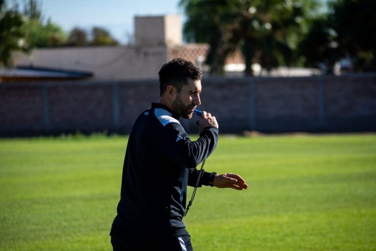 Um árbitro de futebol em uniforme oficial segurando um apito ou um cartão, com um fundo desfocado que sugere um estádio ou documentação oficial.