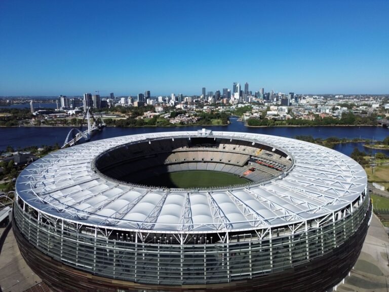 Detalhe das mãos de um torcedor de futebol segurando ou utilizando um objeto engenhoso ou improvisado em um estádio, com a multidão e a estrutura do estádio em segundo plano borrado.