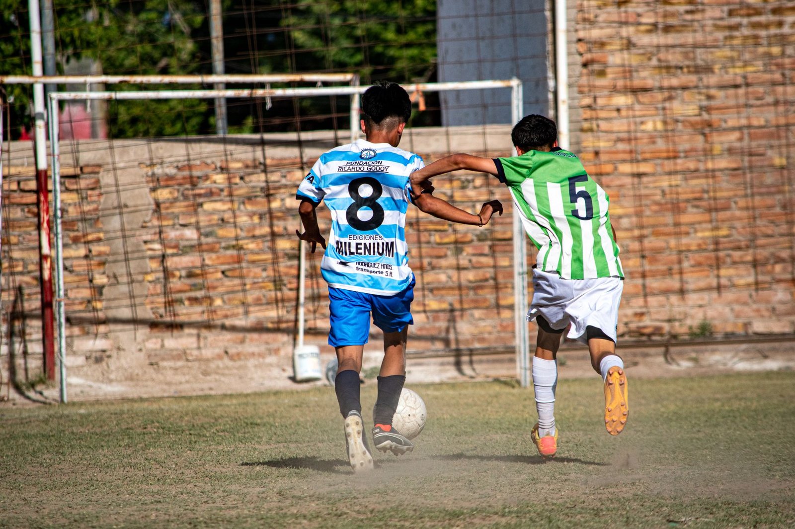 Partida de futebol intensa entre duas equipes de cores distintas (azul e verde) em um grande estádio, com jogadores em ação competitiva disputando a bola.