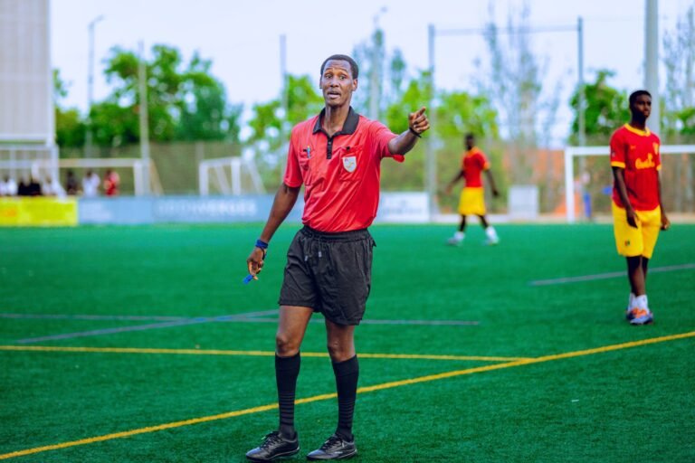 Um árbitro de futebol em campo, fazendo um gesto de decisão durante uma partida profissional, com o gramado verde e o estádio ao fundo, transmitindo autoridade e foco.