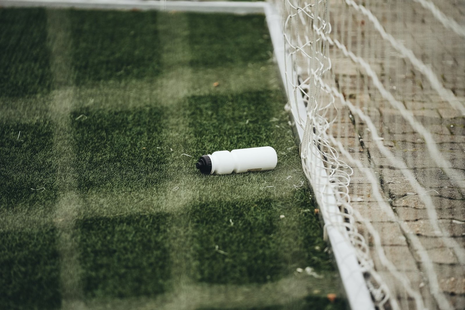Jogadores de futebol tomando água durante uma pausa em campo sob sol intenso, com torcedores observando no estádio