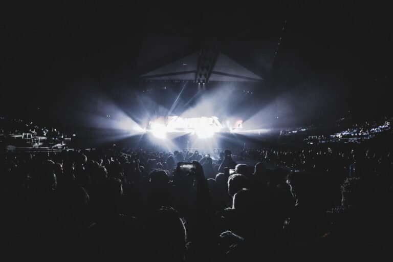 Estádio de futebol iluminado à noite com palco de música, fogos de artifício e torcedores animados