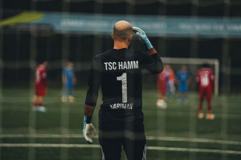 Goleiro de futebol em ação em um estádio, vestindo uma camisa com cores brasileiras, com a torcida ao fundo.