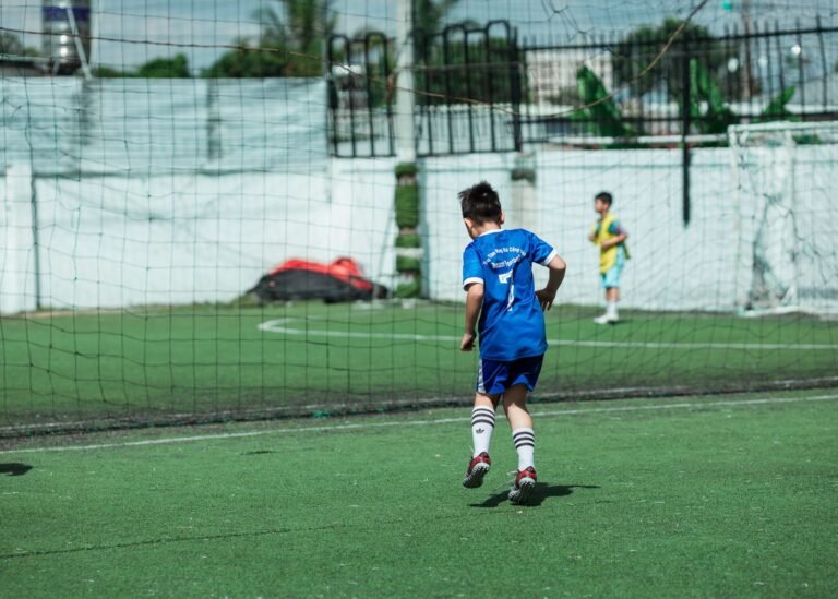 Jovem jogador de futebol celebrando gol em estádio, com torcedores aplaudindo ao fundo.