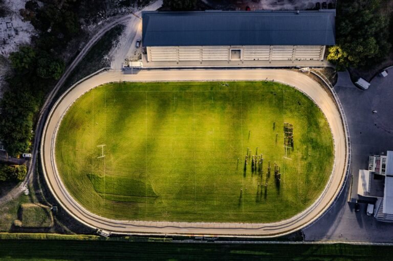 Treinador de futebol em campo de treinamento, falando com jogadores, com bandeira nacional ao fundo.