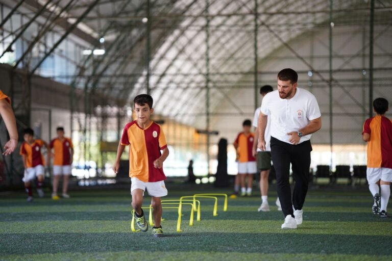 Jovem jogador de futebol retornando ao campo de treinamento, cercado por companheiros e treinadores em uma instalação esportiva moderna