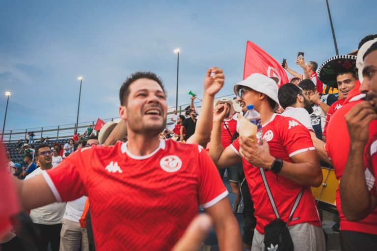 Fãs de futebol egípcios celebrando nas ruas de Cairo, com bandeiras e luzes da cidade.