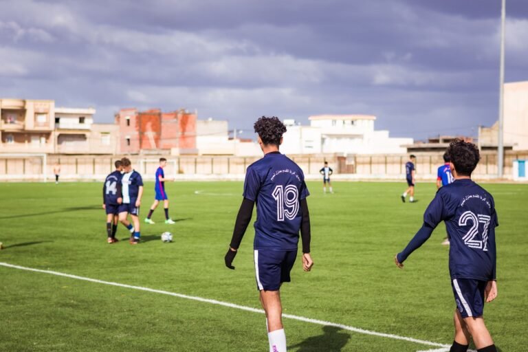 Imagem de um jogo de futebol com a equipe defensiva espanhola em ação, goleiro fazendo uma defesa, e torcida animada no estádio.